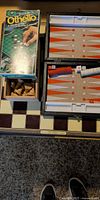 Open foldable board showing backgammon interior, stacked red and white checkers, dice, exterior chessboard pattern, loose chess pieces in box, Pocket Othello package
