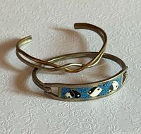 Two Sergio Lub bracelets displayed: yin-yang hinged bangle and twist cuff