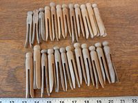 Two rows of wooden one-piece clothes pegs on wood surface, ruler visible