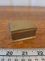 Closed brass stamp box front view next to ruler