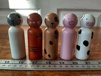 Front view of five wooden animal peg toys aligned beside ruler showing height ~7 cm