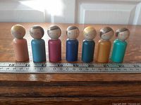 Seven wooden peg figures lined up beside ruler