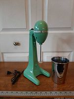 Full view of green Hamilton Beach DrinkMaster with stainless cup and power cord