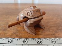 Front view of carved wooden frog guiro with striker inserted
