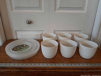 Overall lot showing six white pots and stack of clear saucers