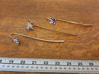 Three brass bookmarks laid flat beside ruler showing length