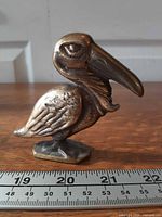 Front left view of brass pelican bottle opener with ruler for scale