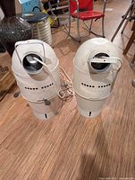 Pair of cylindrical white metal hanging lamps with cords on floor