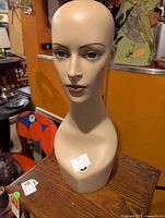 Front view of beige hand-painted mannequin head with elongated neck placed on wooden surface