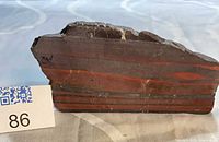 Front polished face showing red jasper bands and martite layers, scale marker 86