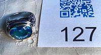 Ring next to lot number showing oval blue topaz and band detail