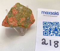 Oblique view of unakite specimen on acrylic stand next to lot tag