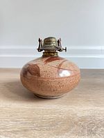 Front view of ceramic oil lamp base showing brass burner and leaf motif