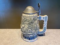 Full view of stein front showing relief scenes, handle, and lid