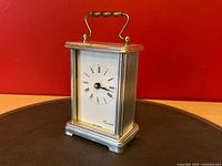 Front view of silver carriage clock on brown surface, red background