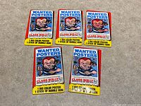 Front view showing five unopened Topps Wanted Posters packs.