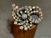 Front view of gold-tone swirl brooch with aurora borealis rhinestones displayed on stand