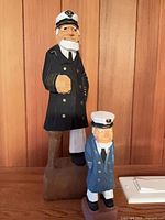 Front view of both wooden sea captain figurines showing painted details and relative sizes