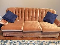 Front view of peach velvet three-seat sofa with two navy pillows