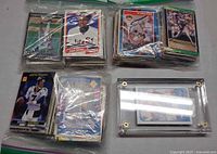 Four bagged stacks of sports cards; top cards show White Sox, Astros, John Elway and card in screw-down case