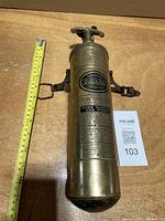 Full view of brass extinguisher with measuring tape and bracket