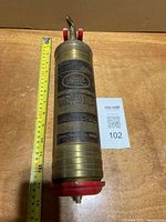 Full view of brass Pyrene extinguisher beside measuring tape and lot card