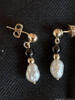 Two gold stud earrings with black beads and pearl drops on black background