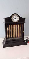 Front view of black mantel clock with analog dial and visible brass chime rods