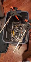 Tote with bar clamps crossed on top, showing quantity of wrenches and hooks inside