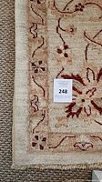 Corner view of beige and rust red floral Chobi rug edge with fringe