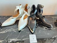 White and black pairs of John Fluevog ankle-strap shoes on table