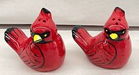 Front view of both red ceramic cardinal shakers showing pour holes and painted details
