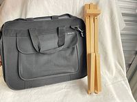 Folding wooden easel beside black Curry's carrying bag.