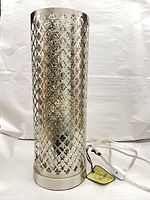 Full view of cylindrical metal lattice lamp with cord and tag