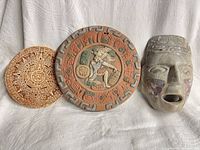 Group shot of three items: calendar plaque, ballgame plaque, stone mask