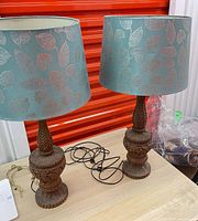 Two carved teak lamps with teal metallic leaf shades on table
