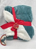 Front view of folded teal throw with white sherpa reverse, red ribbon, hangtags visible
