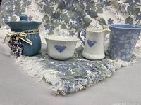 Full lot: miniature creamer, sugar bowl, candle, mug on floral cloth