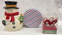 Three items: snowman cookie jar, tree pattern tin, boxed baking cups