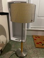Full view of lamp assembled showing metal grid shade, metal and wood stem, round base with switch