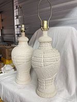 Pair of matching off-white textured ceramic lamps with harps on white backdrop