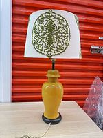 Full view of yellow ceramic lamp with shade attached on table