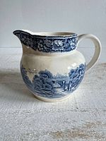 Left side view of pitcher showing blue rural scene and overall shape