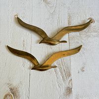 Two brass seagull wall sculptures on white wood background