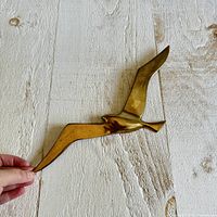 Full view of brass seagull wall hanging against wood background