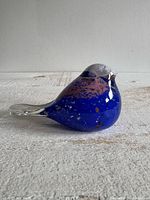 Left profile of art glass bird showing blue body, mottling, clear tail