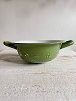 Side view of green enamelware strainer showing perforations and wear