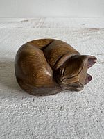 Front view of wooden sleeping cat figurine showing face and curled body