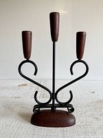 Front view showing black metal scroll arms, central stem, three wooden candle cups, wood base