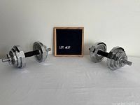 Pair of adjustable chrome dumbbells beside small sign